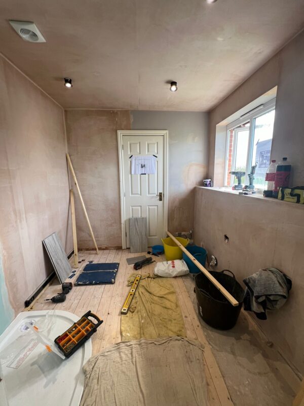 Room with bare plaster walls, bare wooden floor and various building supplies.