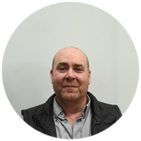 Phil bald middle aged man with stubble smiling, in grey shirt and black jacket.